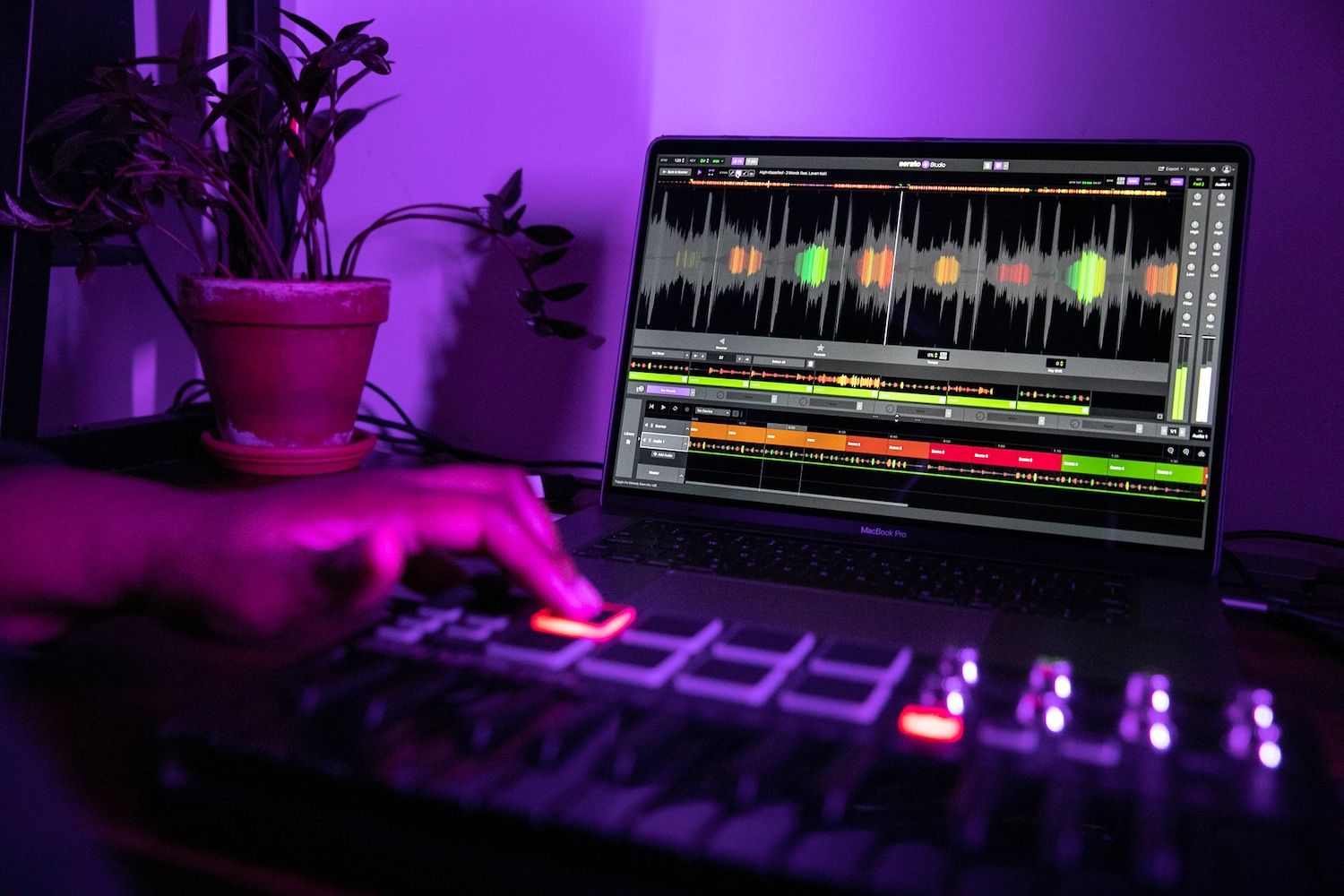 Serato Studio 2.0 on a laptop computer in purple room with a hand in the foreground triggering a cuepoint on a MIDI controller