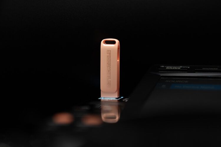 A rose gold colored USB drive with the DJ Techtools logo on it plugged into a CDJ